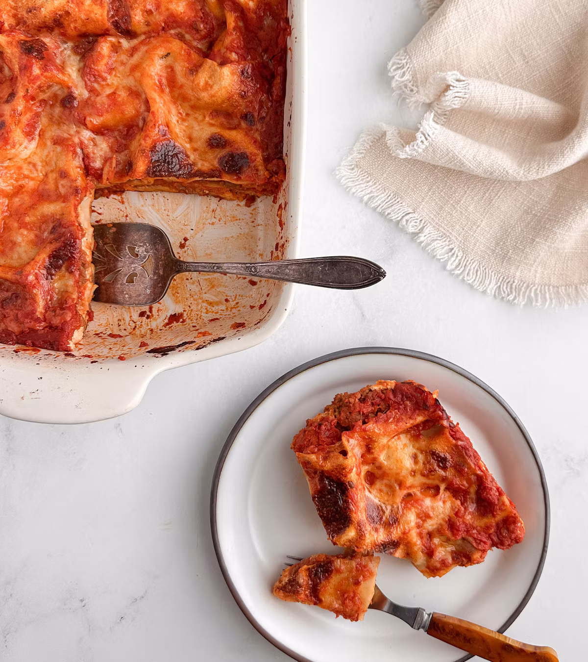 A baking dish of lasagna with one slice served on a plate beside it.