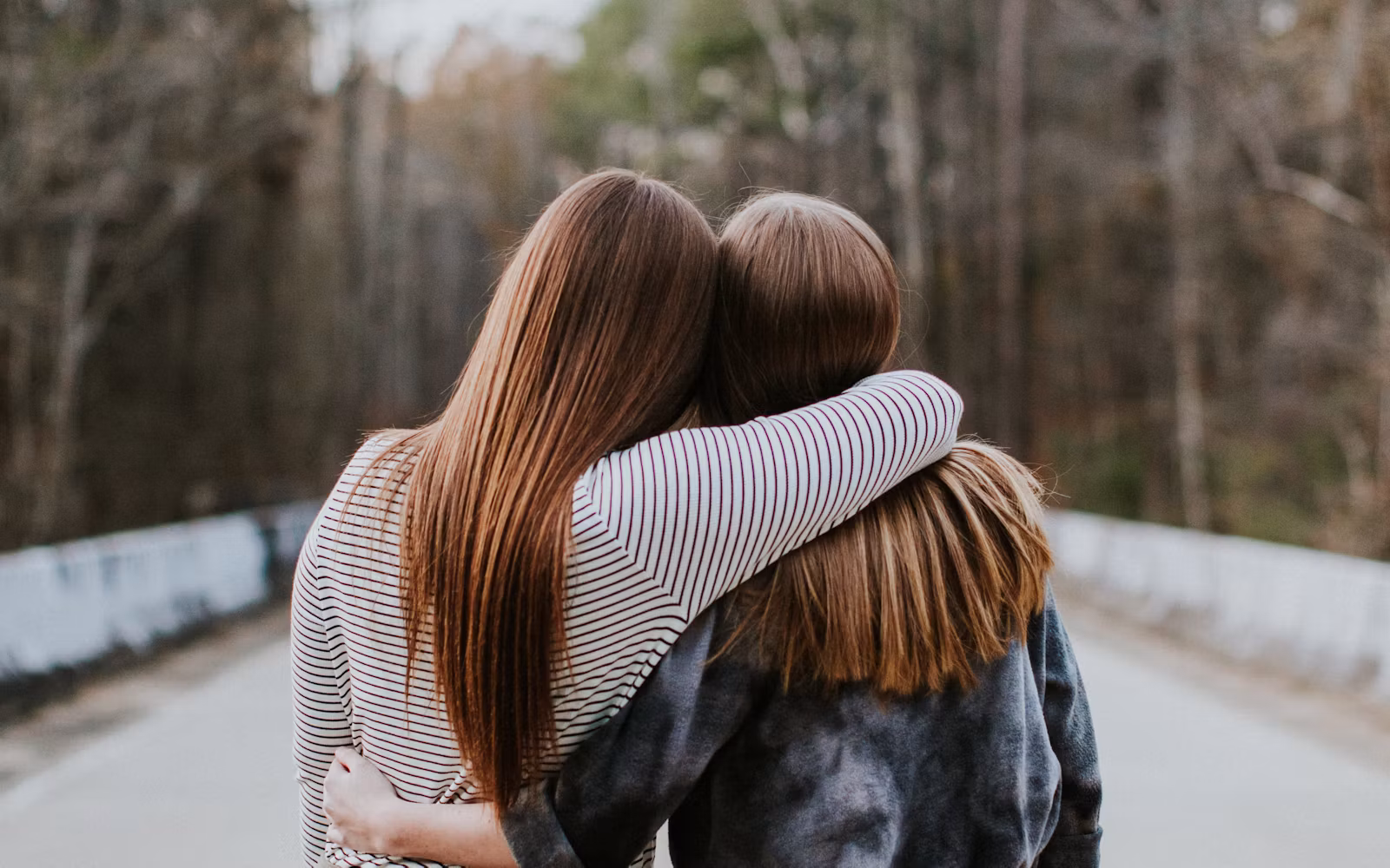 Two friends walking down a wooded road with their arms around each other.