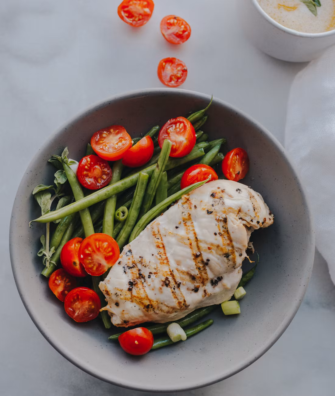 A bowl of grilled chicken with green beans and cherry tomatoes.