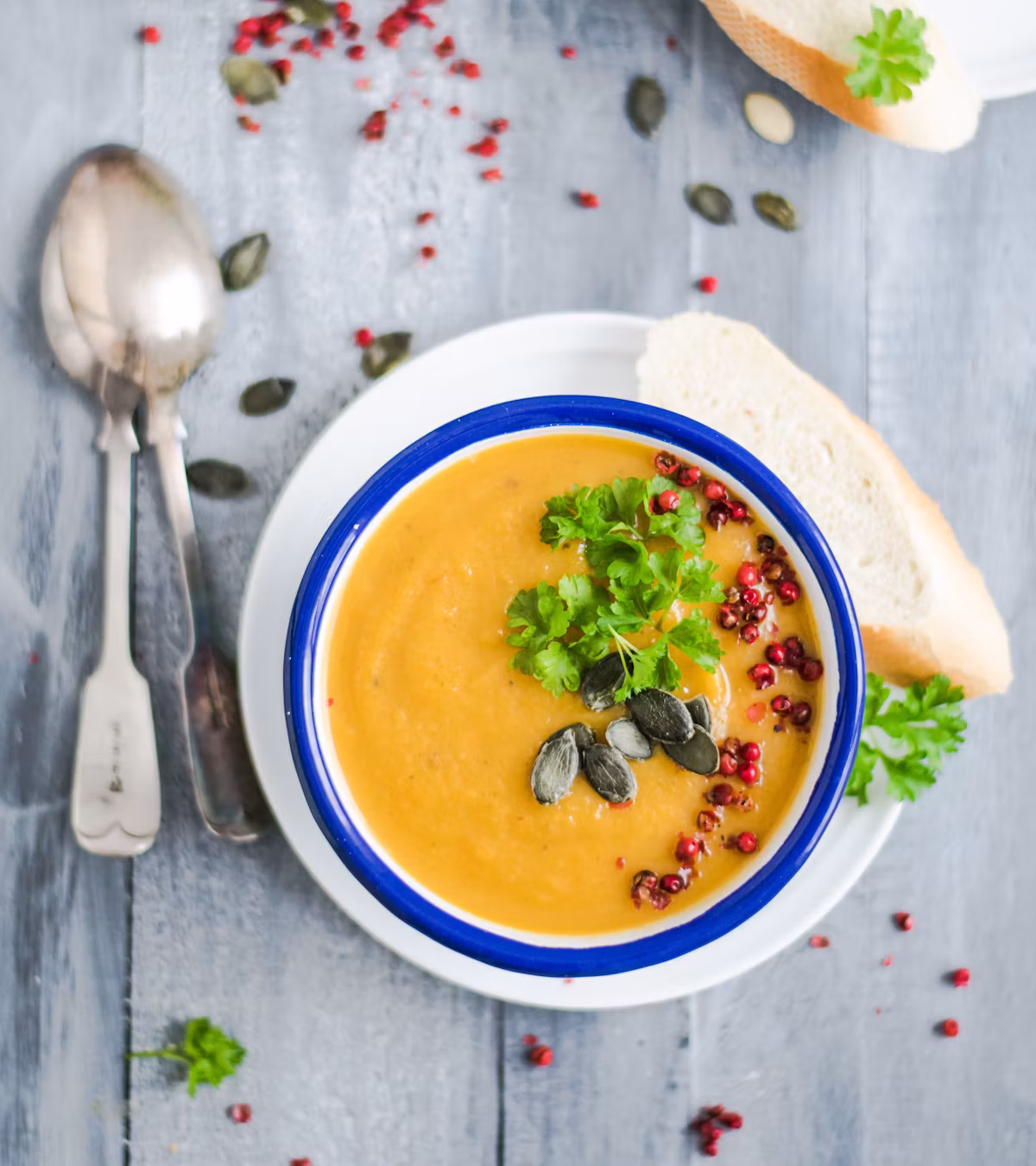 A bowl of creamy orange soup topped with herbs and pumpkin seeds, with bread on the side.
